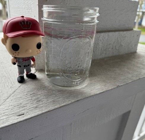 Pop! Freddy Funko (Baseball) next to a cylinder/glass of water.